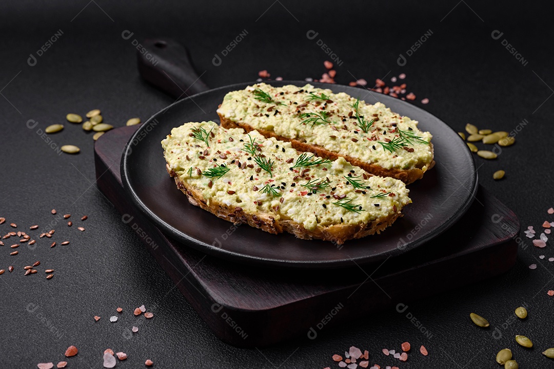Torradas grelhadas com pasta de abacate, ovos, cream cheese, sal, especiarias e ervas sobre uma mesa de concreto texturizado