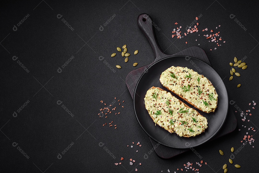 Torradas grelhadas com pasta de abacate, ovos, cream cheese, sal, especiarias e ervas sobre uma mesa de concreto texturizado