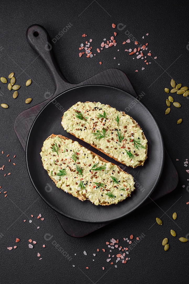 Torradas grelhadas com pasta de abacate, ovos, cream cheese, sal, especiarias e ervas sobre uma mesa de concreto texturizado