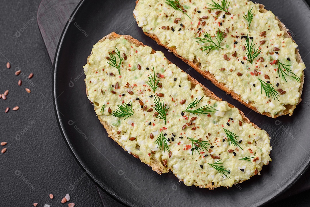 Torradas grelhadas com pasta de abacate, ovos, cream cheese, sal, especiarias e ervas sobre uma mesa de concreto texturizado