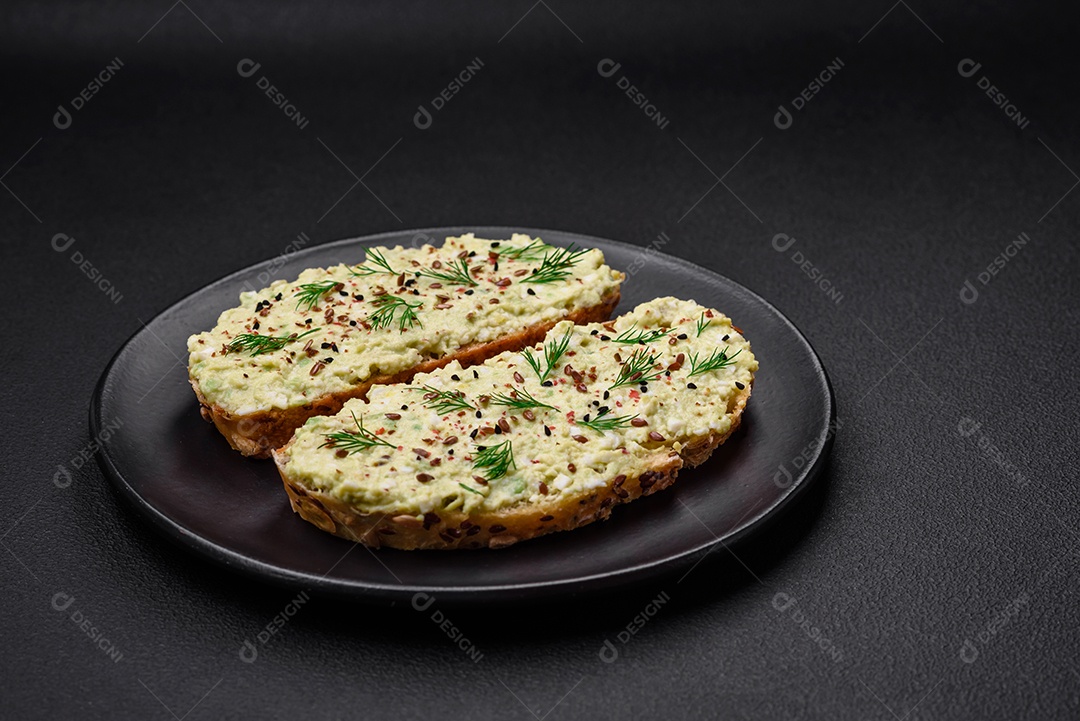 Torradas grelhadas com pasta de abacate, ovos, cream cheese, sal, especiarias e ervas sobre uma mesa de concreto texturizado