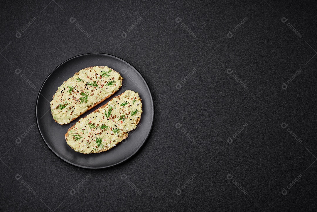Torradas grelhadas com pasta de abacate, ovos, cream cheese, sal, especiarias e ervas sobre uma mesa de concreto texturizado