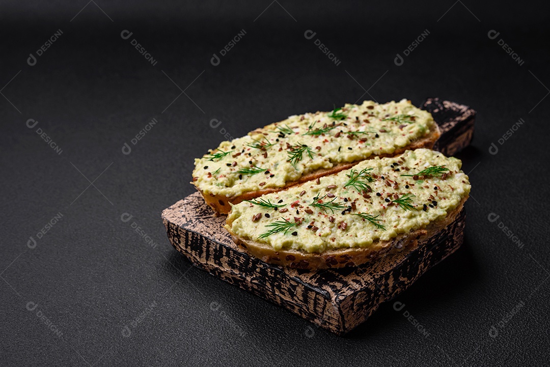 Torradas grelhadas com pasta de abacate, ovos, cream cheese, sal, especiarias e ervas sobre uma mesa de concreto texturizado
