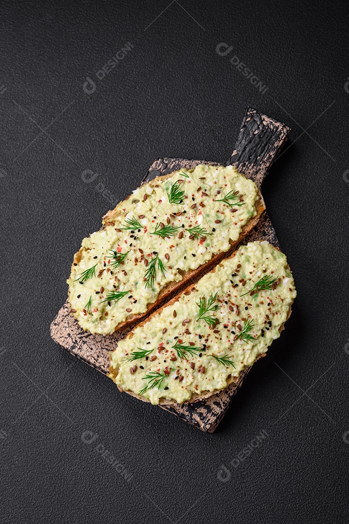 Torradas grelhadas com pasta de abacate, ovos, cream cheese, sal, especiarias e ervas sobre uma mesa de concreto texturizado