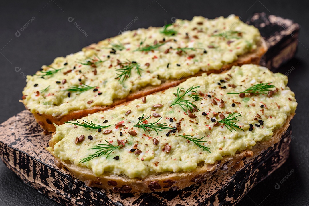 Torradas grelhadas com pasta de abacate, ovos, cream cheese, sal, especiarias e ervas sobre uma mesa de concreto texturizado