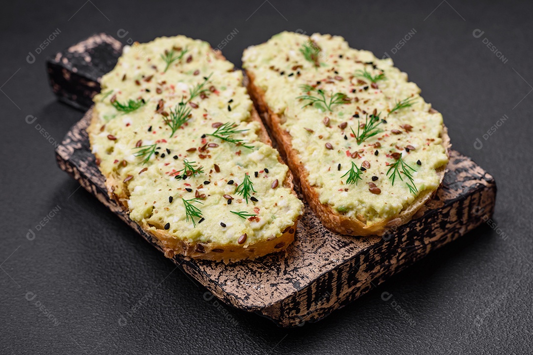 Torradas grelhadas com pasta de abacate, ovos, cream cheese, sal, especiarias e ervas sobre uma mesa de concreto texturizado