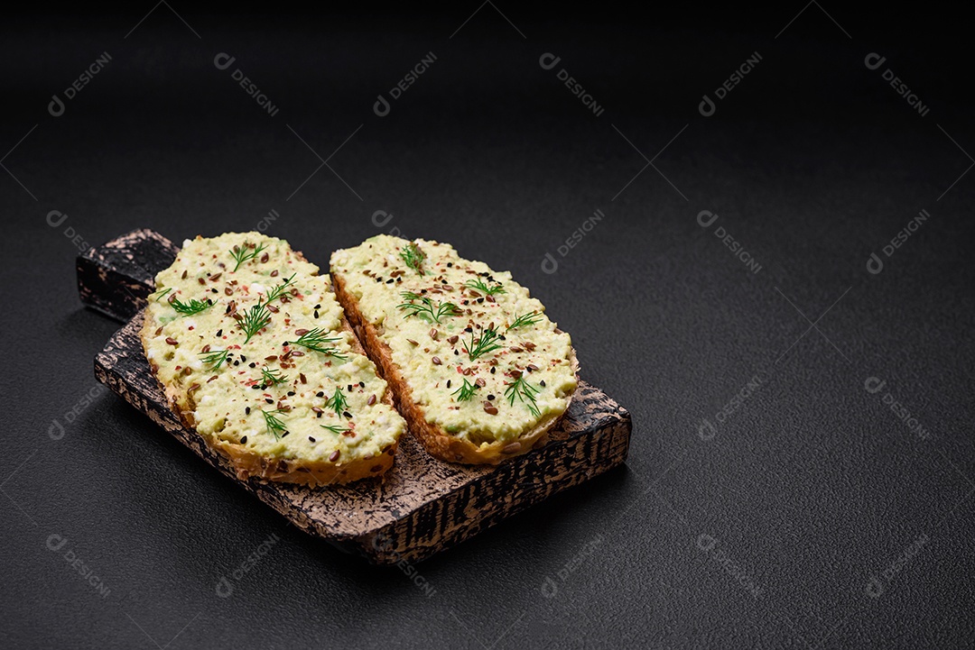 Torradas grelhadas com pasta de abacate, ovos, cream cheese, sal, especiarias e ervas sobre uma mesa de concreto texturizado