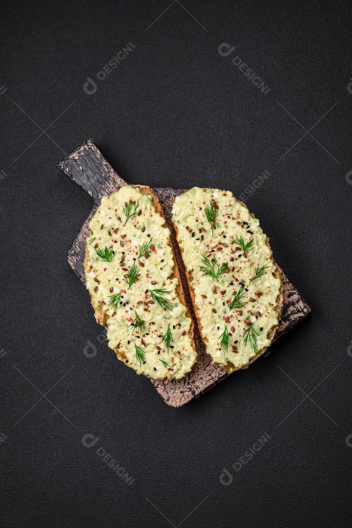 Torradas grelhadas com pasta de abacate, ovos, cream cheese, sal, especiarias e ervas sobre uma mesa de concreto texturizado