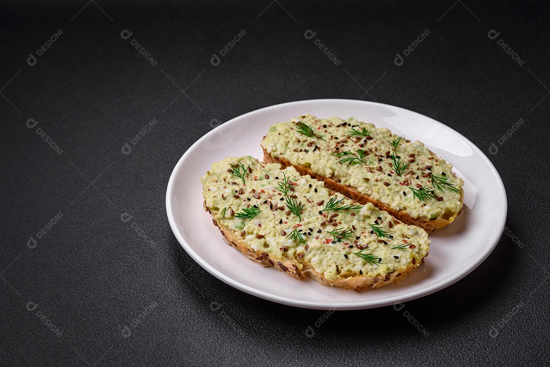 Torradas grelhadas com pasta de abacate, ovos, cream cheese, sal, especiarias e ervas sobre uma mesa de concreto texturizado