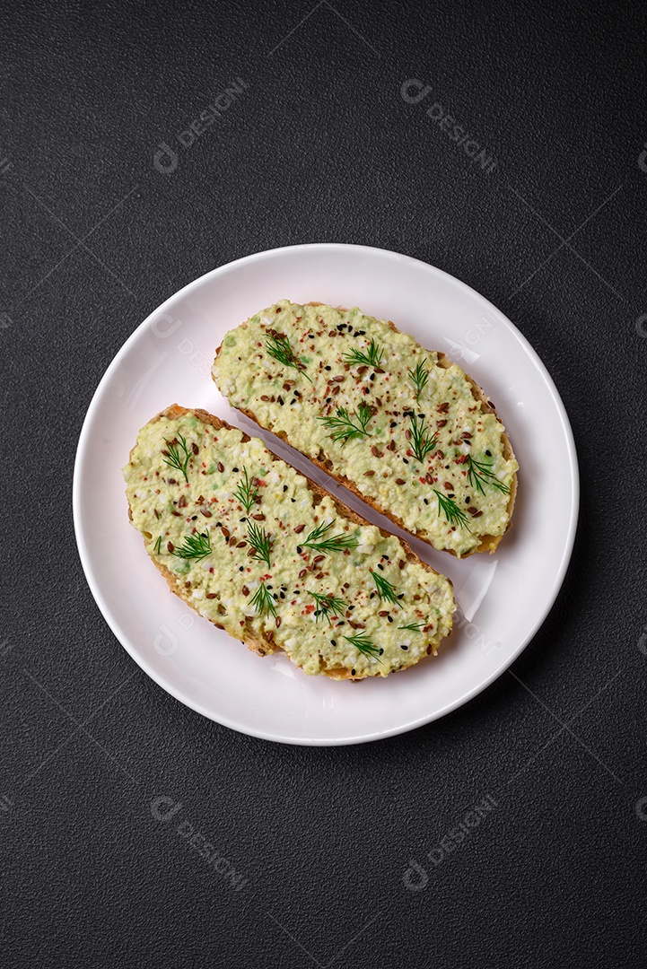 Torradas grelhadas com pasta de abacate, ovos, cream cheese, sal, especiarias e ervas sobre uma mesa de concreto texturizado