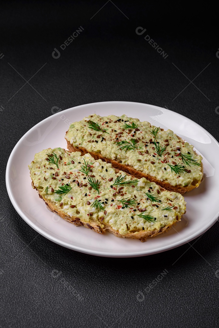 Torradas grelhadas com pasta de abacate, ovos, cream cheese, sal, especiarias e ervas sobre uma mesa de concreto texturizado