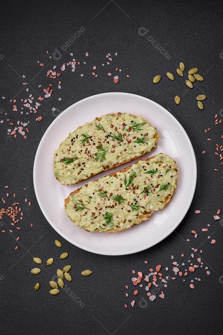 Torradas grelhadas com pasta de abacate, ovos, cream cheese, sal, especiarias e ervas sobre uma mesa de concreto texturizado