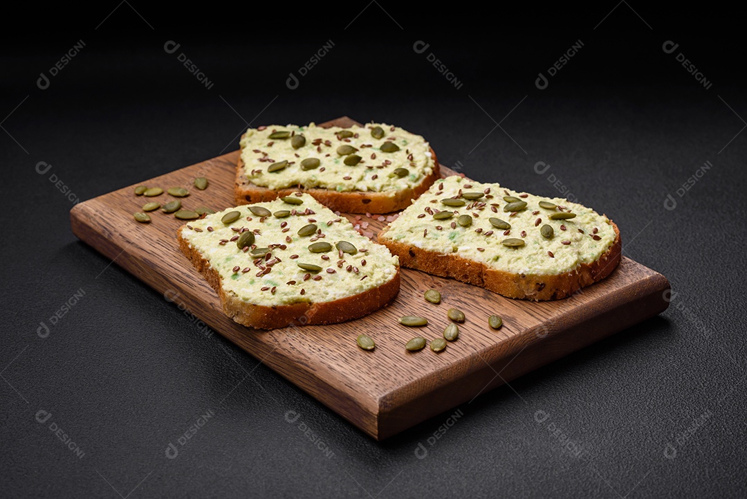 Torradas grelhadas com pasta de abacate, ovos, cream cheese, sal, especiarias e ervas sobre uma mesa de concreto texturizado