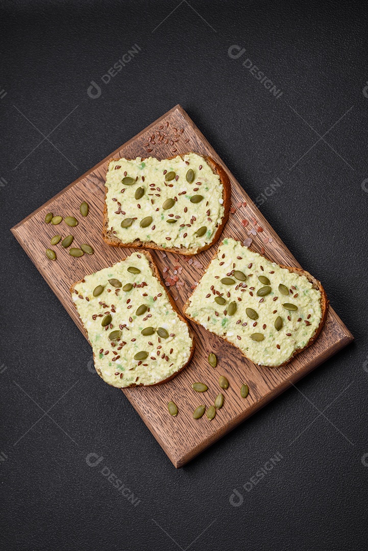 Torradas grelhadas com pasta de abacate, ovos, cream cheese, sal, especiarias e ervas sobre uma mesa de concreto texturizado