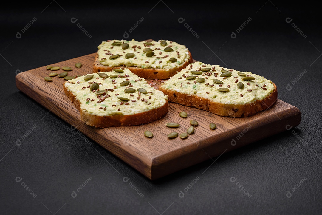 Torradas grelhadas com pasta de abacate, ovos, cream cheese, sal, especiarias e ervas sobre uma mesa de concreto texturizado