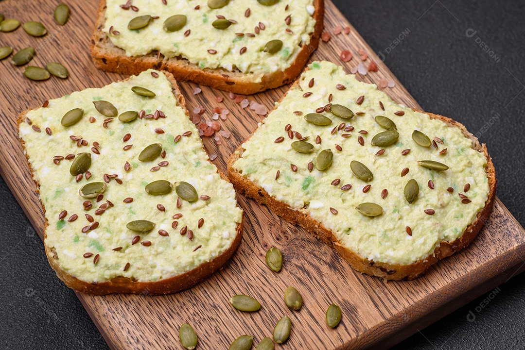Torradas grelhadas com pasta de abacate, ovos, cream cheese, sal, especiarias e ervas sobre uma mesa de concreto texturizado