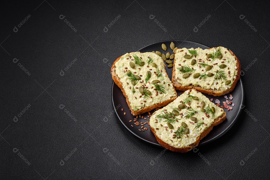 Torradas grelhadas com pasta de abacate, ovos, cream cheese, sal, especiarias e ervas sobre uma mesa de concreto texturizado