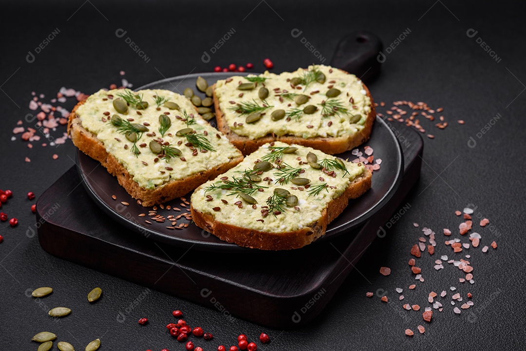 Torradas grelhadas com pasta de abacate, ovos, cream cheese, sal, especiarias e ervas sobre uma mesa de concreto texturizado