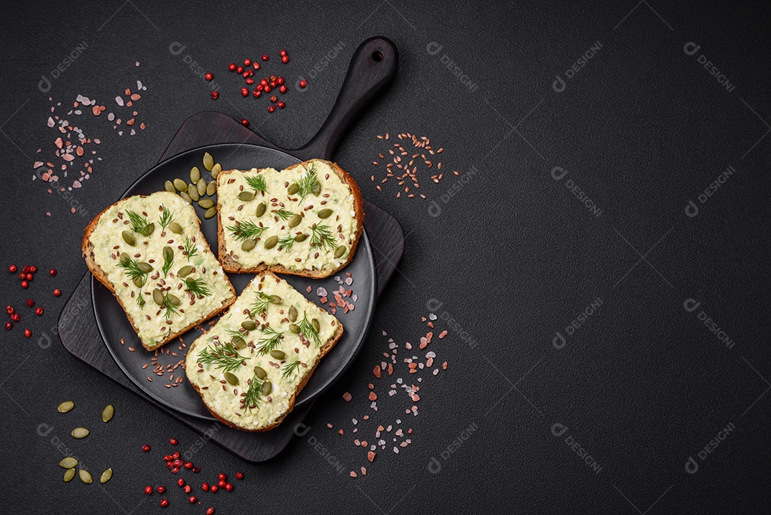 Torradas grelhadas com pasta de abacate, ovos, cream cheese, sal, especiarias e ervas sobre uma mesa de concreto texturizado