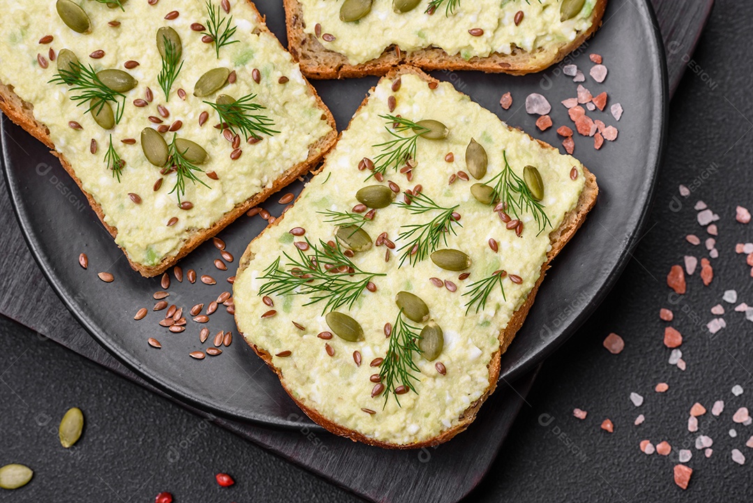 Torradas grelhadas com pasta de abacate, ovos, cream cheese, sal, especiarias e ervas sobre uma mesa de concreto texturizado