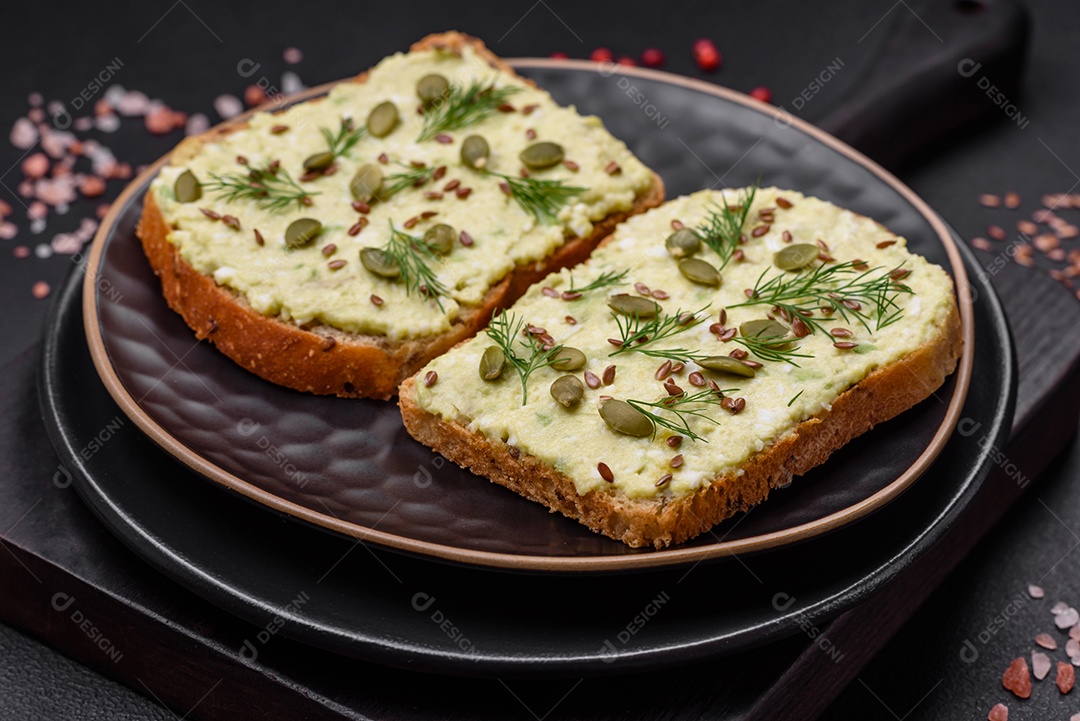 Torradas grelhadas com pasta de abacate, ovos, cream cheese, sal, especiarias e ervas sobre uma mesa de concreto texturizado