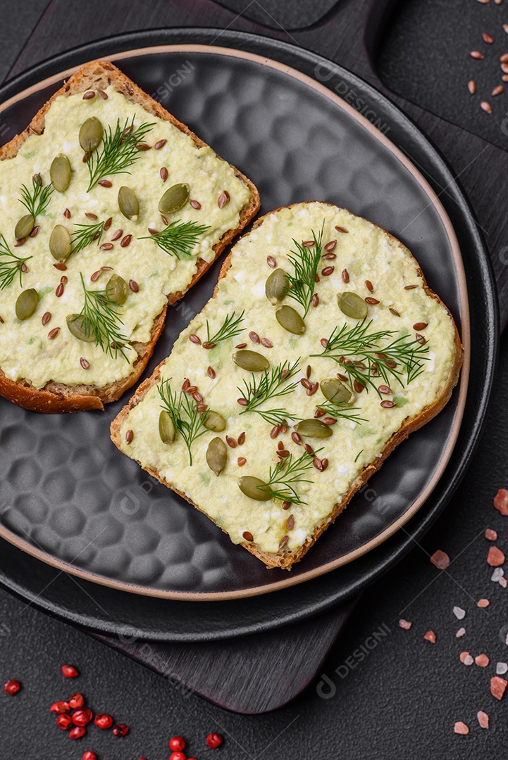 Torradas grelhadas com pasta de abacate, ovos, cream cheese, sal, especiarias e ervas sobre uma mesa de concreto texturizado