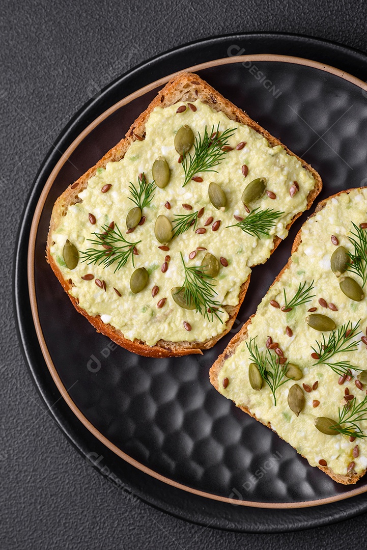 Torradas grelhadas com pasta de abacate, ovos, cream cheese, sal, especiarias e ervas sobre uma mesa de concreto texturizado