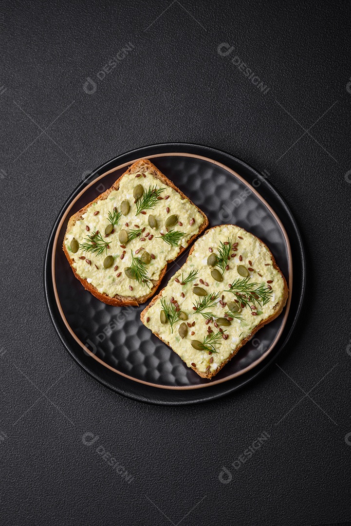 Torradas grelhadas com pasta de abacate, ovos, cream cheese, sal, especiarias e ervas sobre uma mesa de concreto texturizado