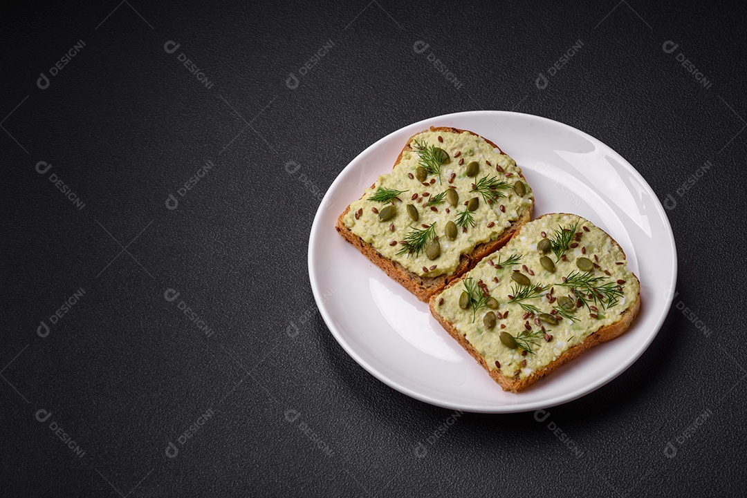 Torradas grelhadas com pasta de abacate, ovos, cream cheese, sal, especiarias e ervas sobre uma mesa de concreto texturizado