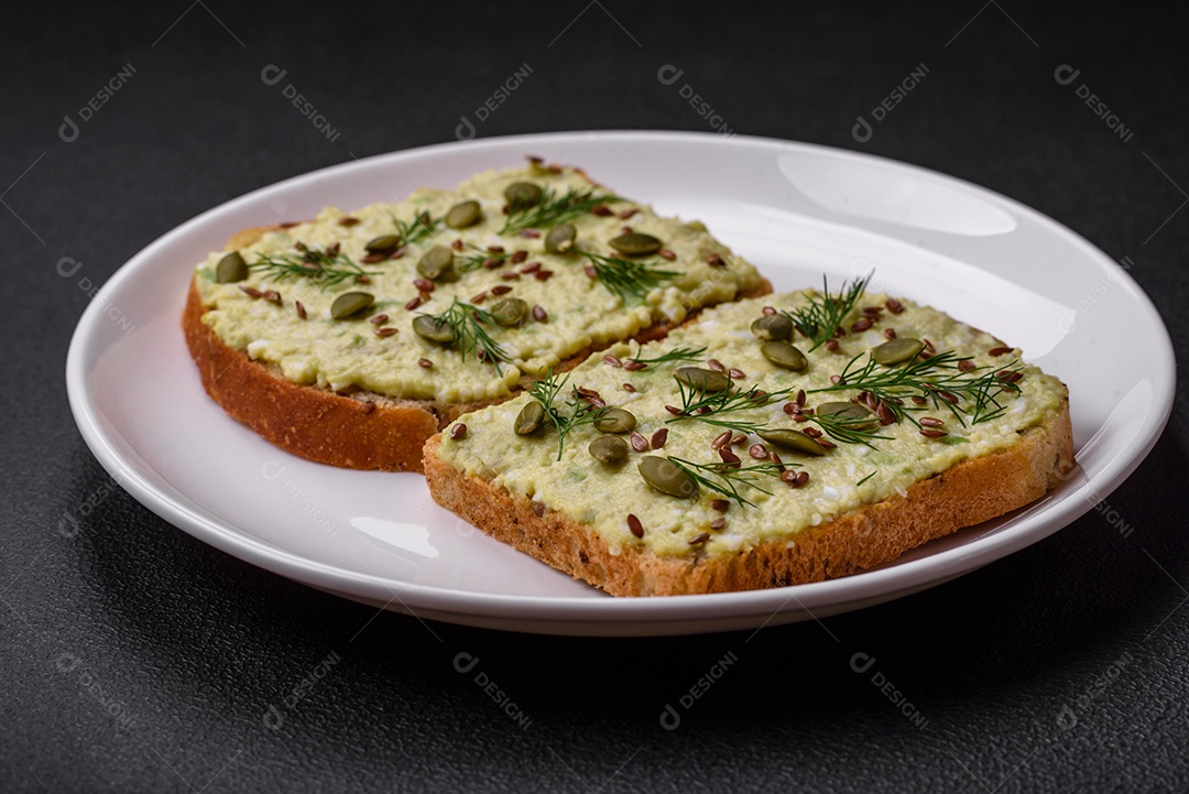 Torradas grelhadas com pasta de abacate, ovos, cream cheese, sal, especiarias e ervas sobre uma mesa de concreto texturizado