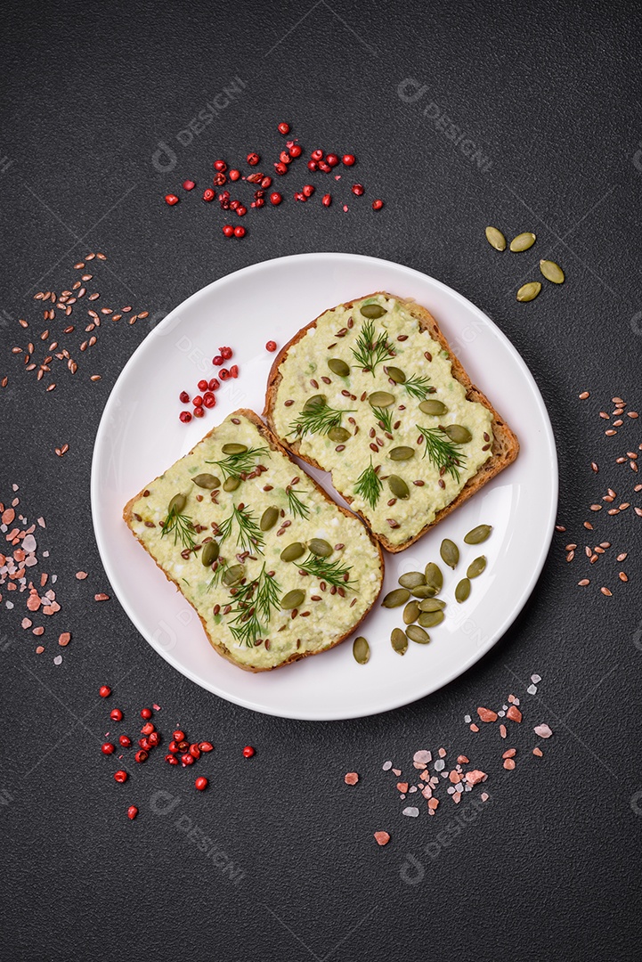 Torradas grelhadas com pasta de abacate, ovos, cream cheese, sal, especiarias e ervas sobre uma mesa de concreto texturizado