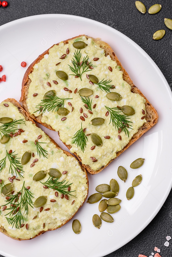 Torradas grelhadas com pasta de abacate, ovos, cream cheese, sal, especiarias e ervas sobre uma mesa de concreto texturizado