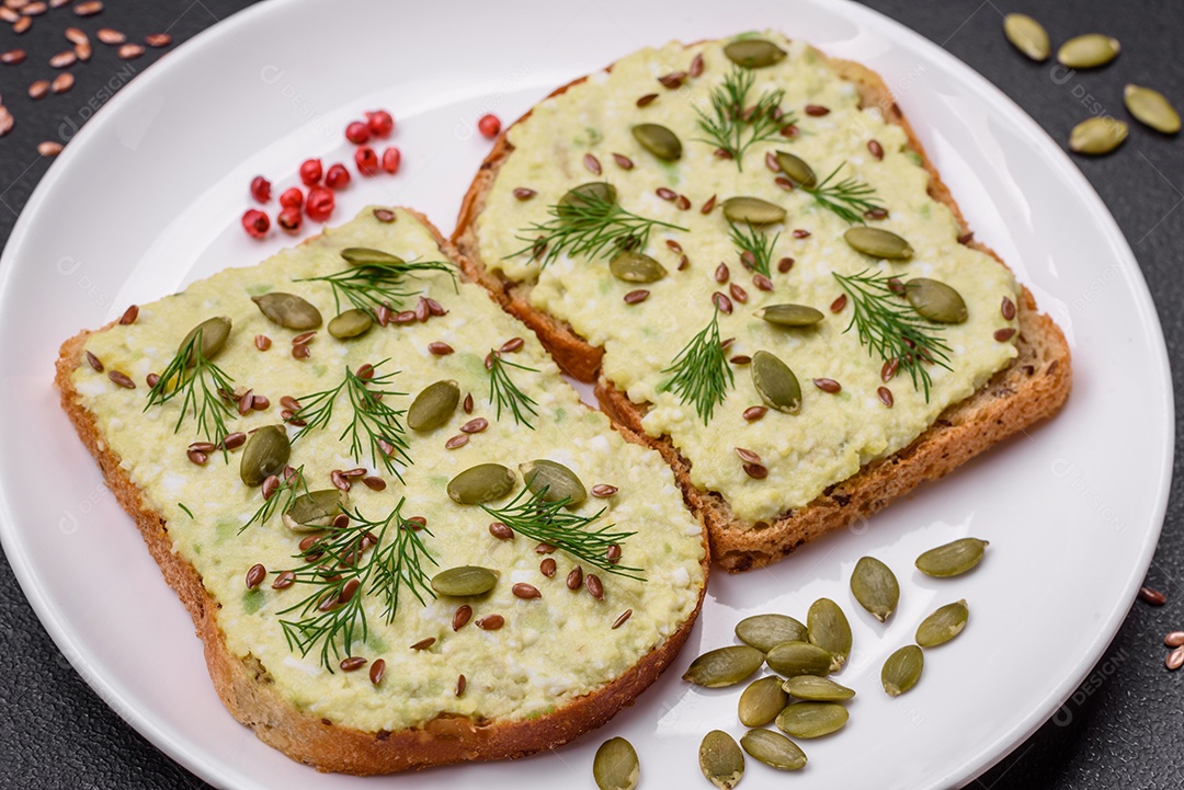 Torradas grelhadas com pasta de abacate, ovos, cream cheese, sal, especiarias e ervas sobre uma mesa de concreto texturizado