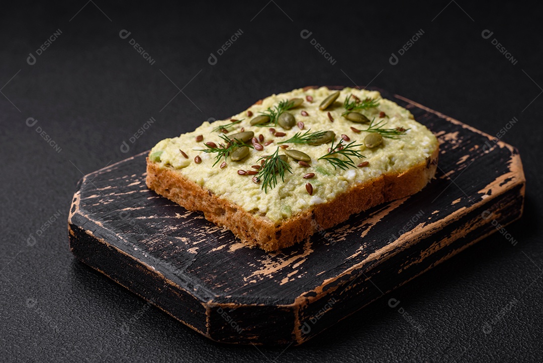 Torradas grelhadas com pasta de abacate, ovos, cream cheese, sal, especiarias e ervas sobre uma mesa de concreto texturizado