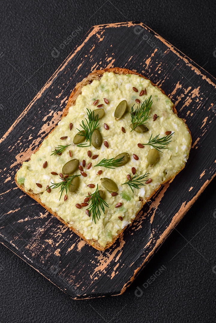 Torradas grelhadas com pasta de abacate, ovos, cream cheese, sal, especiarias e ervas sobre uma mesa de concreto texturizado