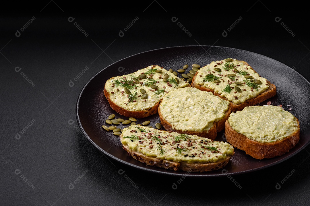 Torradas grelhadas com pasta de abacate, ovos, cream cheese, sal, especiarias e ervas sobre uma mesa de concreto texturizado