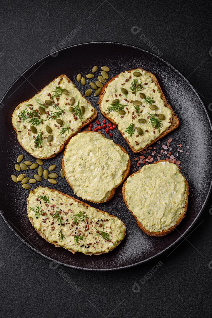 Torradas grelhadas com pasta de abacate, ovos, cream cheese, sal, especiarias e ervas sobre uma mesa de concreto texturizado
