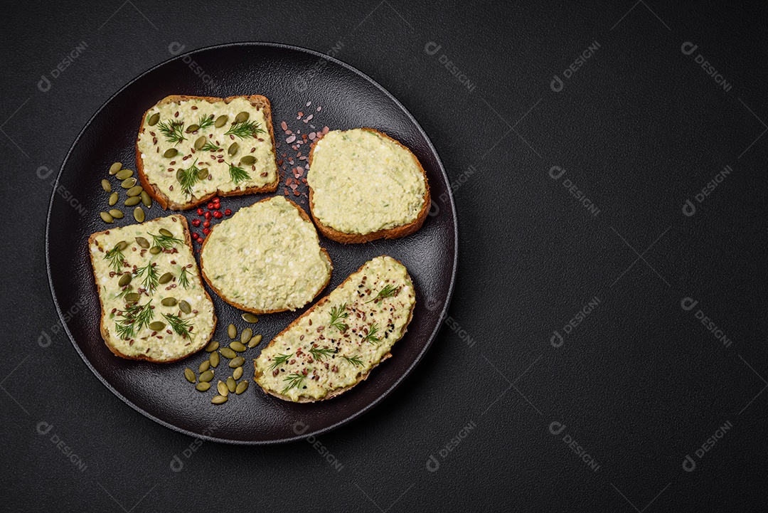 Torradas grelhadas com pasta de abacate, ovos, cream cheese, sal, especiarias e ervas sobre uma mesa de concreto texturizado