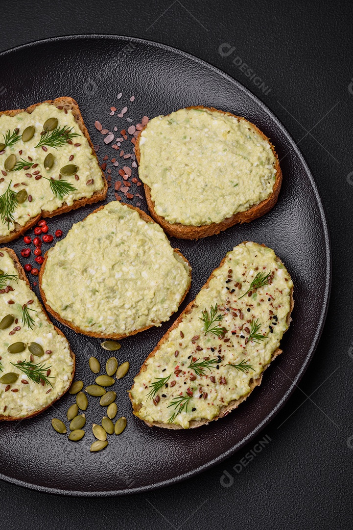 Torradas grelhadas com pasta de abacate, ovos, cream cheese, sal, especiarias e ervas sobre uma mesa de concreto texturizado