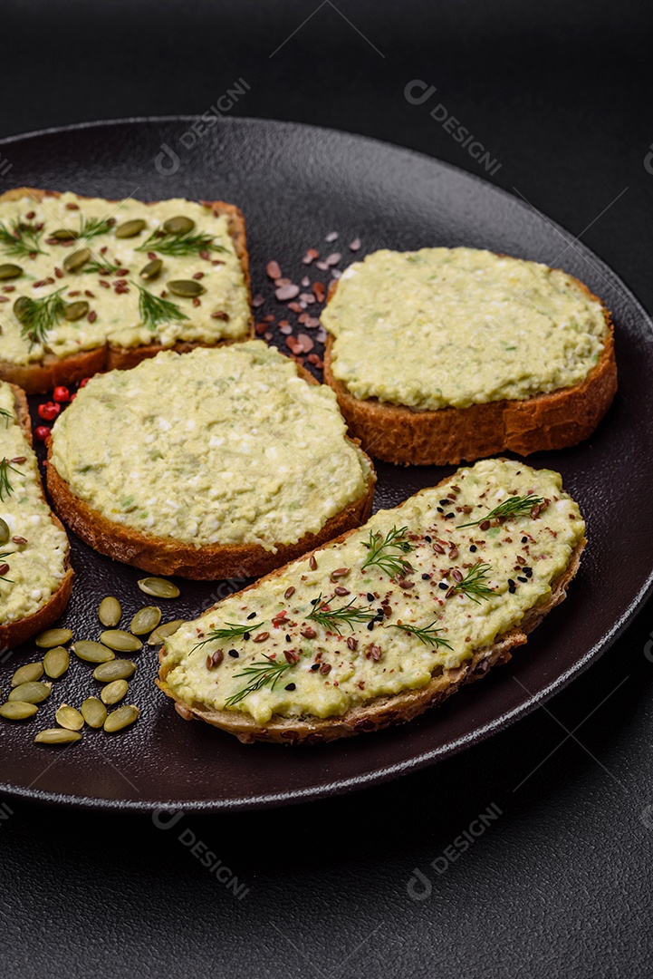 Torradas grelhadas com pasta de abacate, ovos, cream cheese, sal, especiarias e ervas sobre uma mesa de concreto texturizado