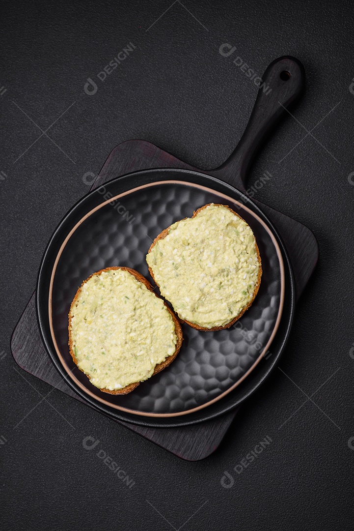 Torradas grelhadas com pasta de abacate, ovos, cream cheese, sal, especiarias e ervas sobre uma mesa de concreto texturizado