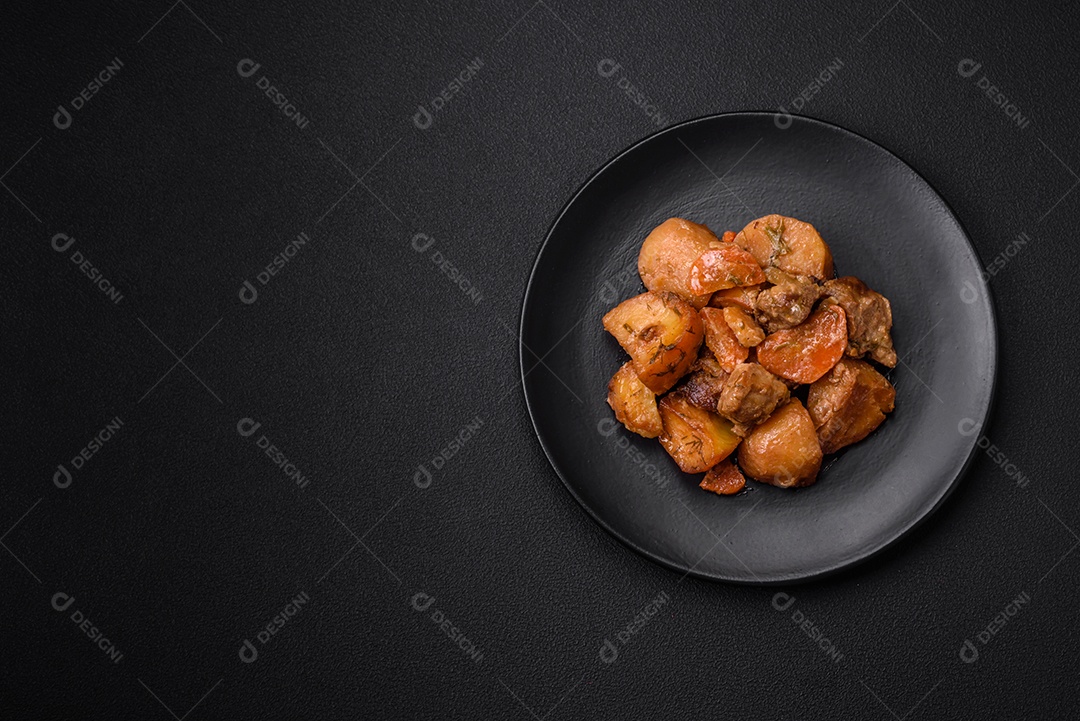 Delicioso ensopado fresco cozido com carne de porco ou carne bovina com batatas, cenouras, especiarias e ervas sobre um fundo escuro de concreto