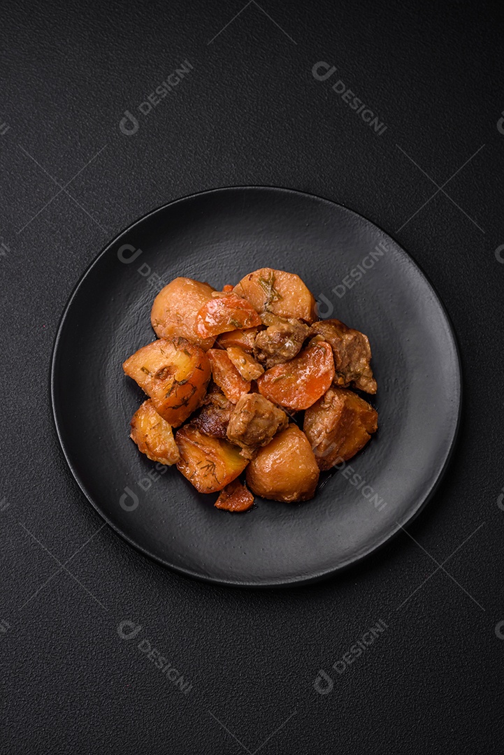 Delicioso ensopado fresco cozido com carne de porco ou carne bovina com batatas, cenouras, especiarias e ervas sobre um fundo escuro de concreto