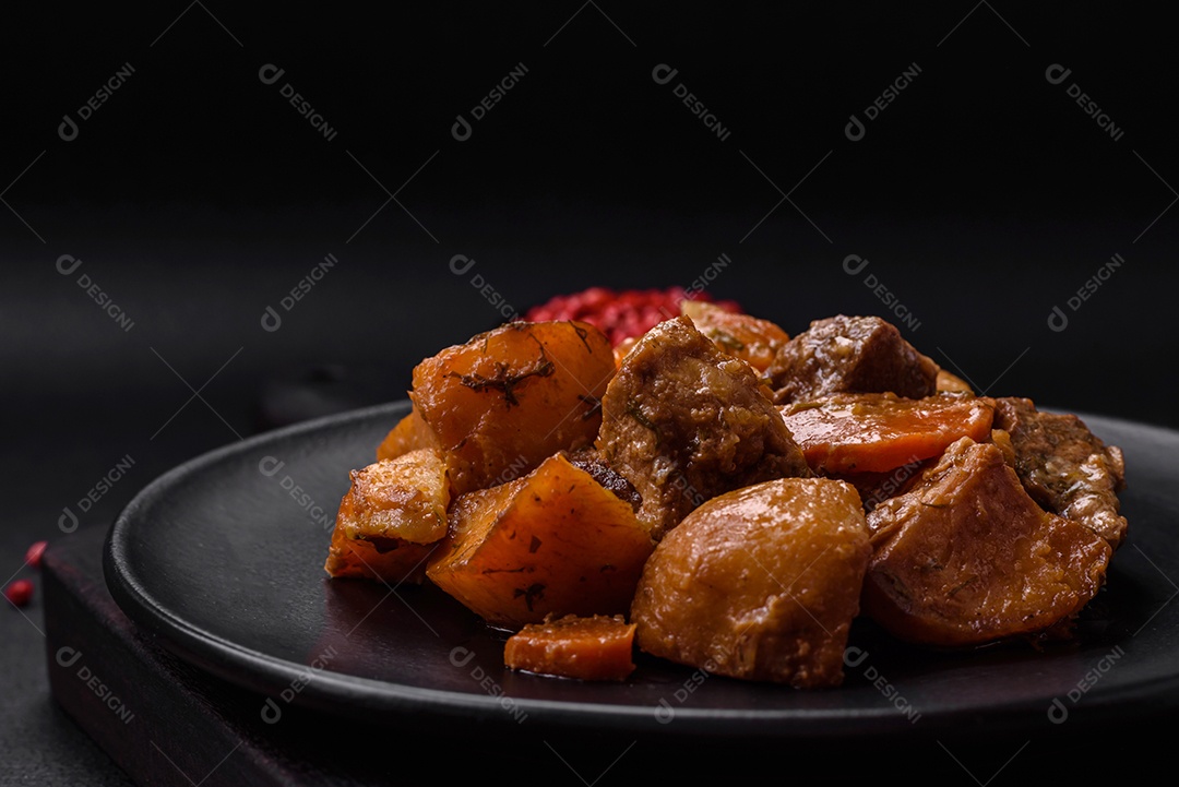 Delicioso ensopado fresco cozido com carne de porco ou carne bovina com batatas, cenouras, especiarias e ervas sobre um fundo escuro de concreto