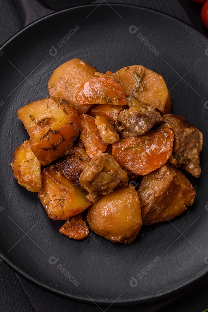 Delicioso ensopado fresco cozido com carne de porco ou carne bovina com batatas, cenouras, especiarias e ervas sobre um fundo escuro de concreto