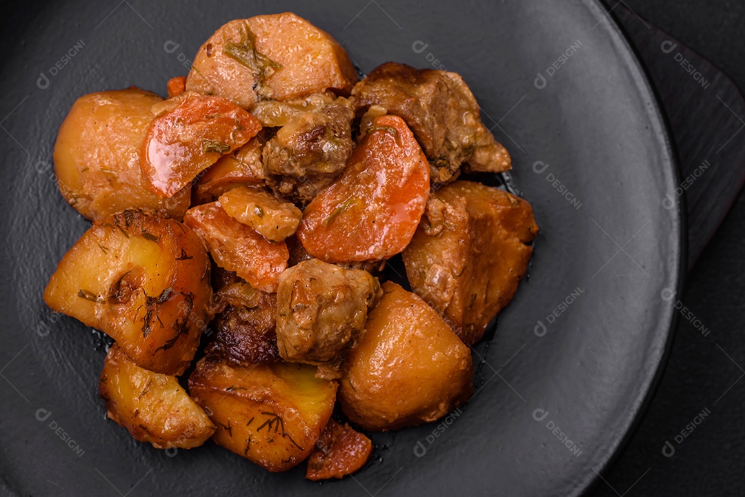 Delicioso ensopado fresco cozido com carne de porco ou carne bovina com batatas, cenouras, especiarias e ervas sobre um fundo escuro de concreto