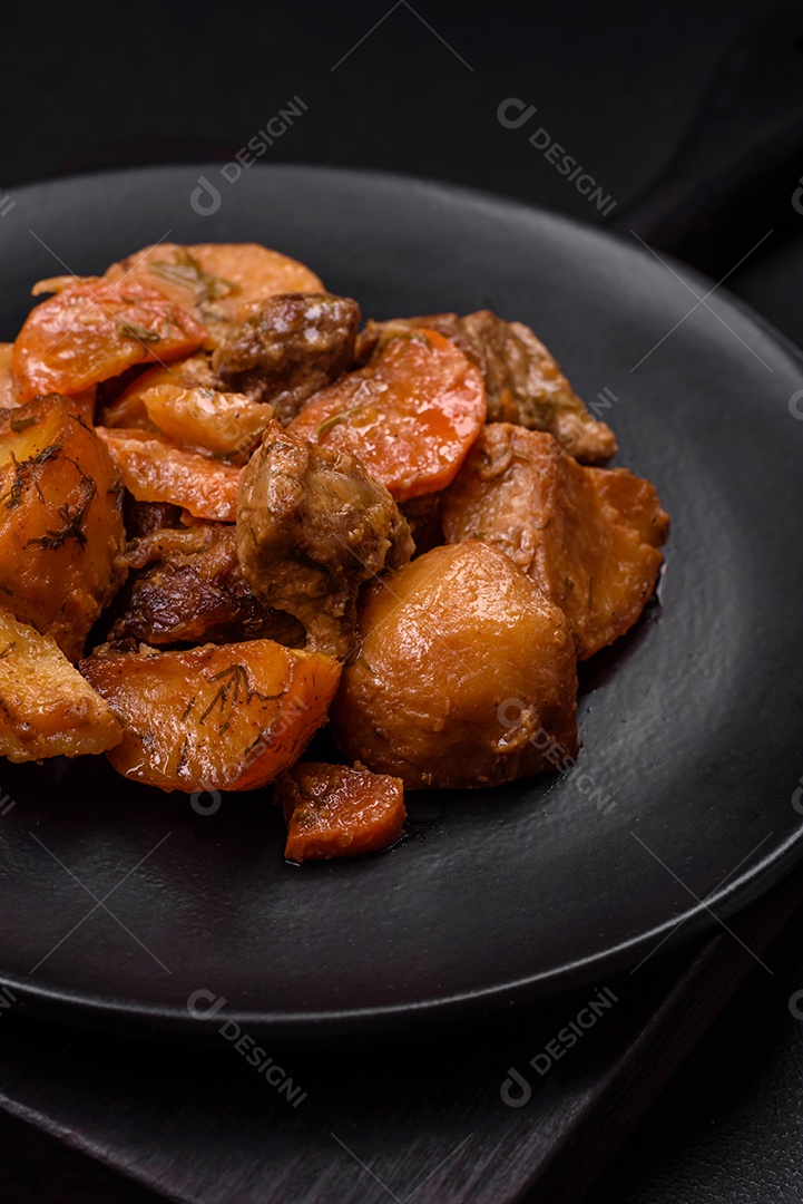 Delicioso ensopado fresco cozido com carne de porco ou carne bovina com batatas, cenouras, especiarias e ervas sobre um fundo escuro de concreto