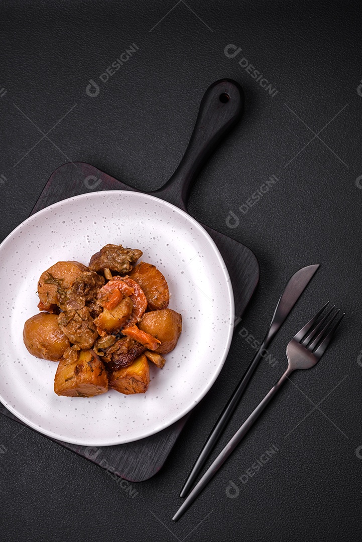 Delicioso ensopado fresco cozido com carne de porco ou carne bovina com batatas, cenouras, especiarias e ervas sobre um fundo escuro de concreto