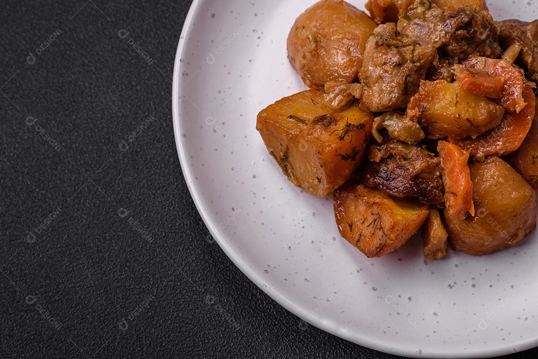 Delicioso ensopado fresco cozido com carne de porco ou carne bovina com batatas, cenouras, especiarias e ervas sobre um fundo escuro de concreto