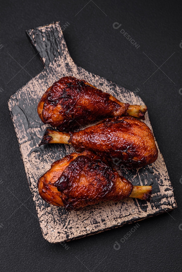 Deliciosas pernas de frango grelhado com especiarias e ervas em molho teriyaki sobre um fundo escuro de concreto